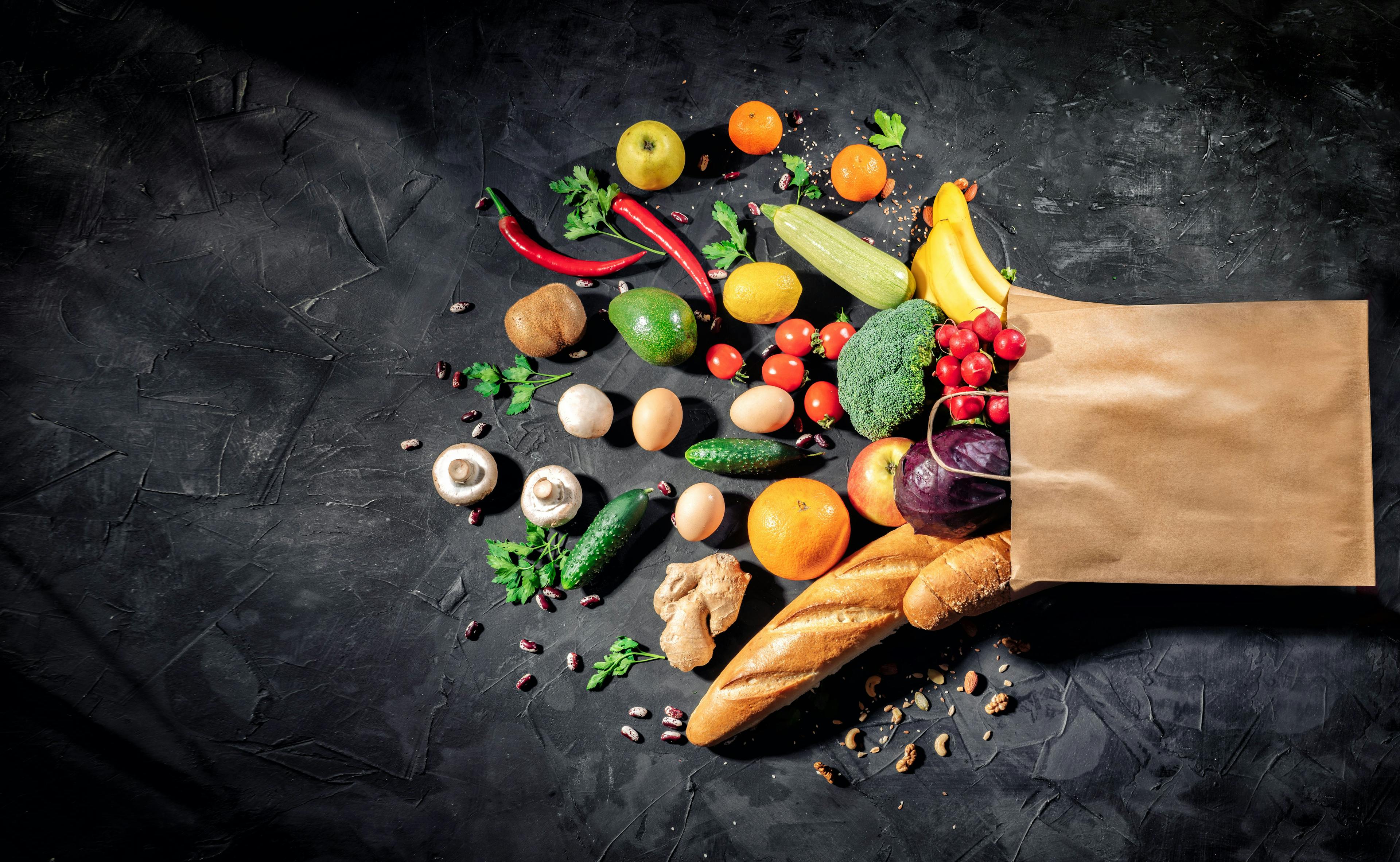 Healthy food in full paper bag of different products vegetables and fruits on dark background | Image Credit: © Andrii - stock.adobe.com