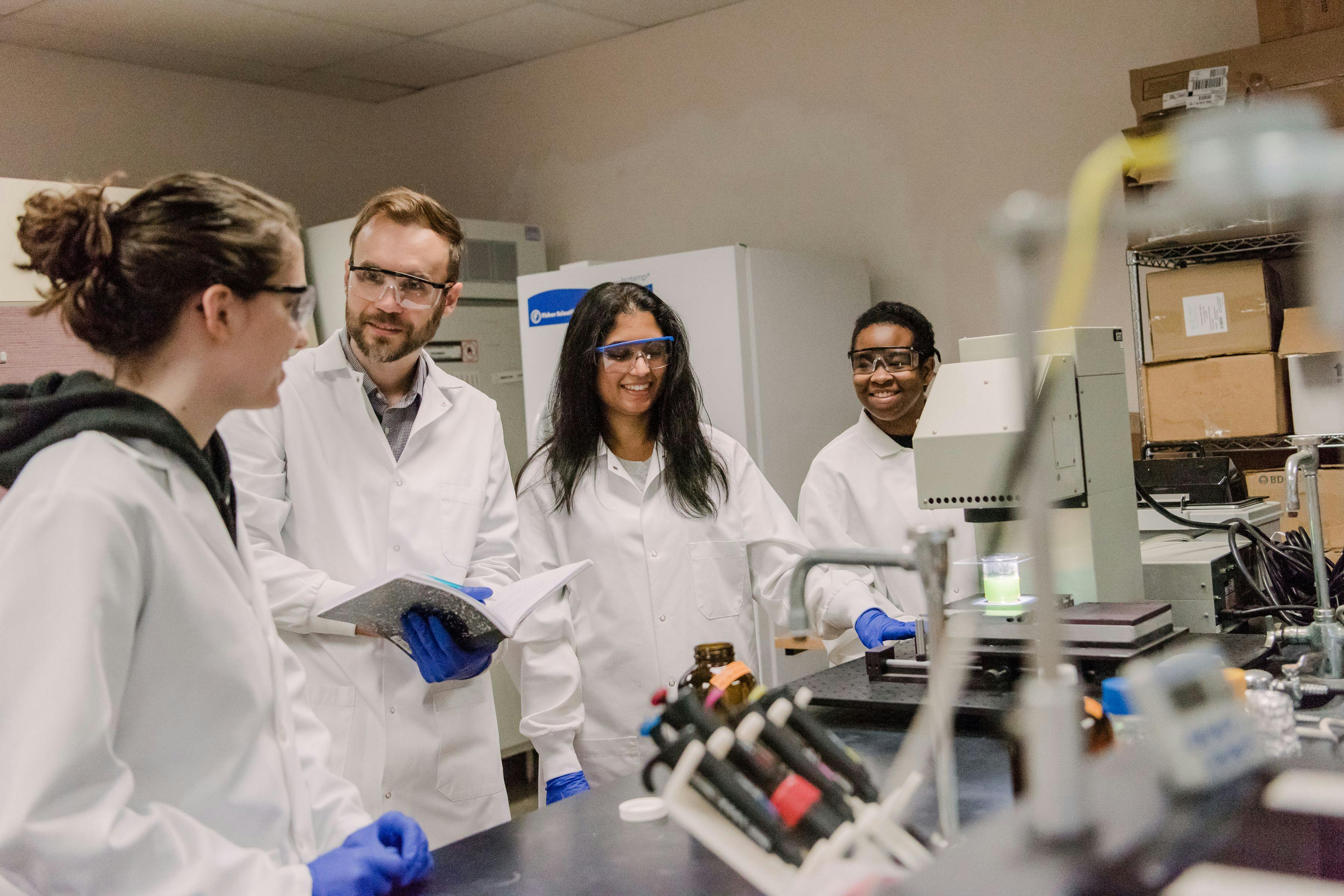 Blaney (second from left) with undergraduate researchers Bridget Anger (left) and Lauren Harris (right) and PhD candidate Mamatha Hopanna (second from right) discuss photochemical treatment of antibiotics in water. Photo Credit: © Lee Blaney