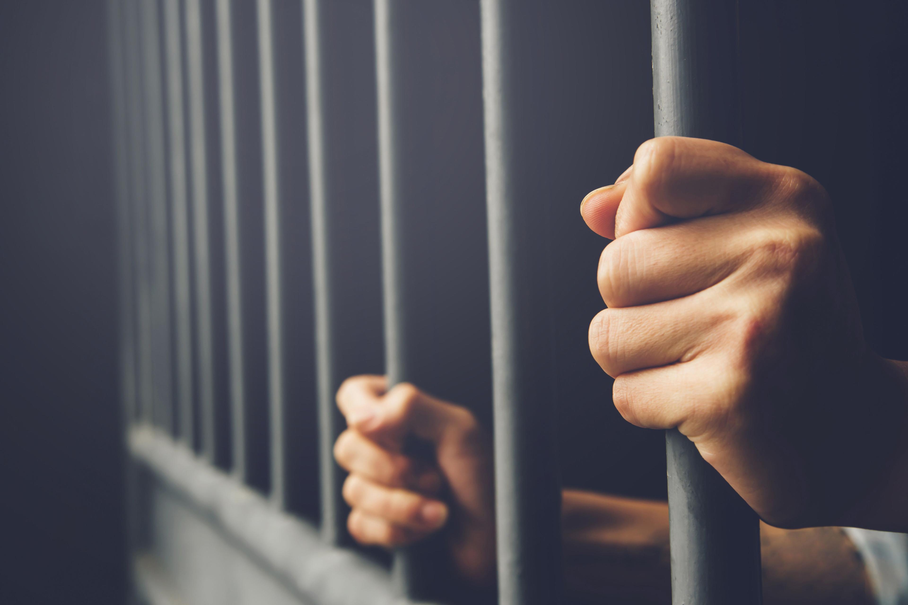 Man in prison hold steel cage jail bars. © methaphum - stock.adobe.com