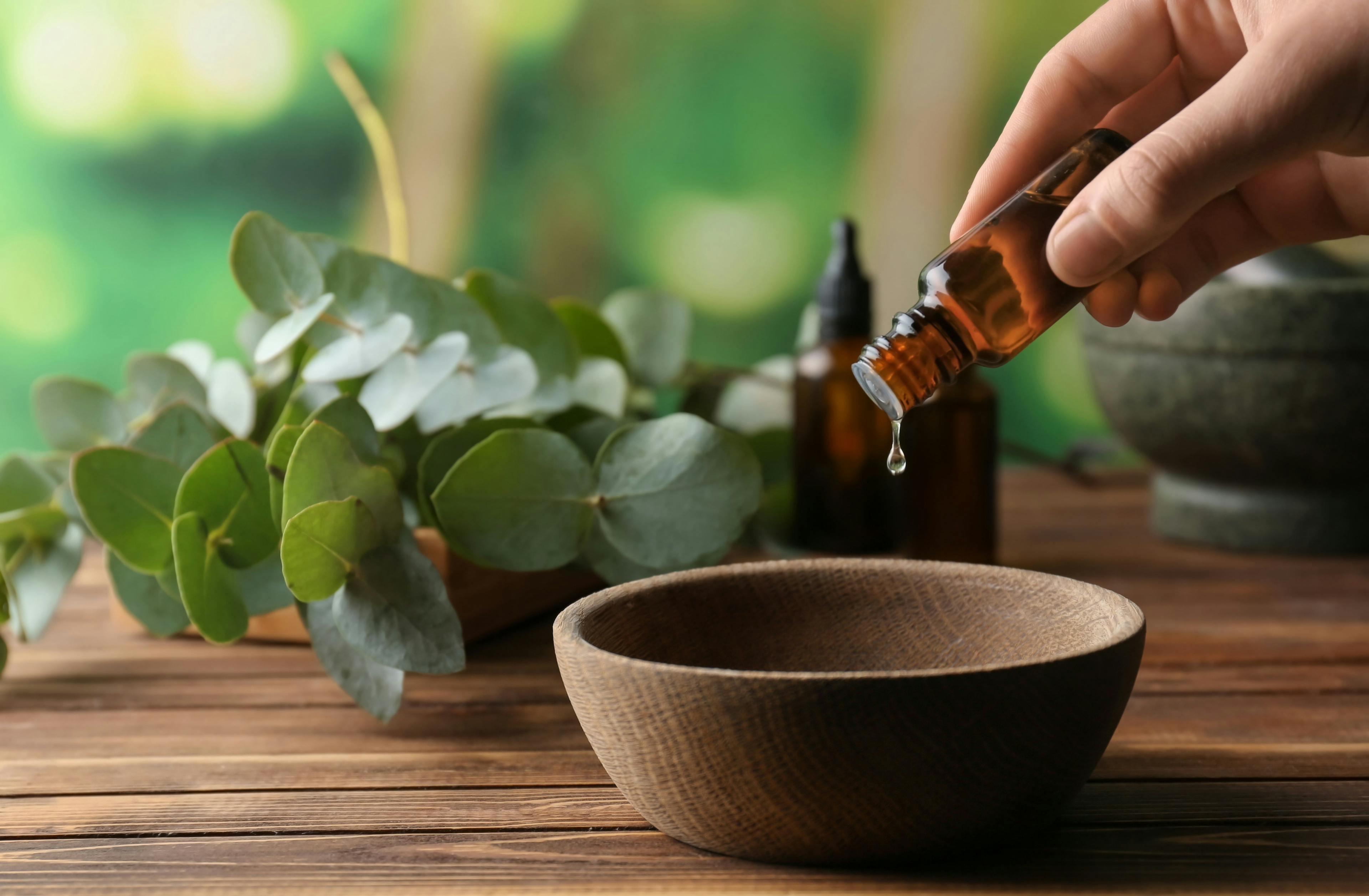 Woman pouring eucalyptus essential oil into bowl on wooden table | Image Credit: © Pixel-Shot - stock.adobe.com