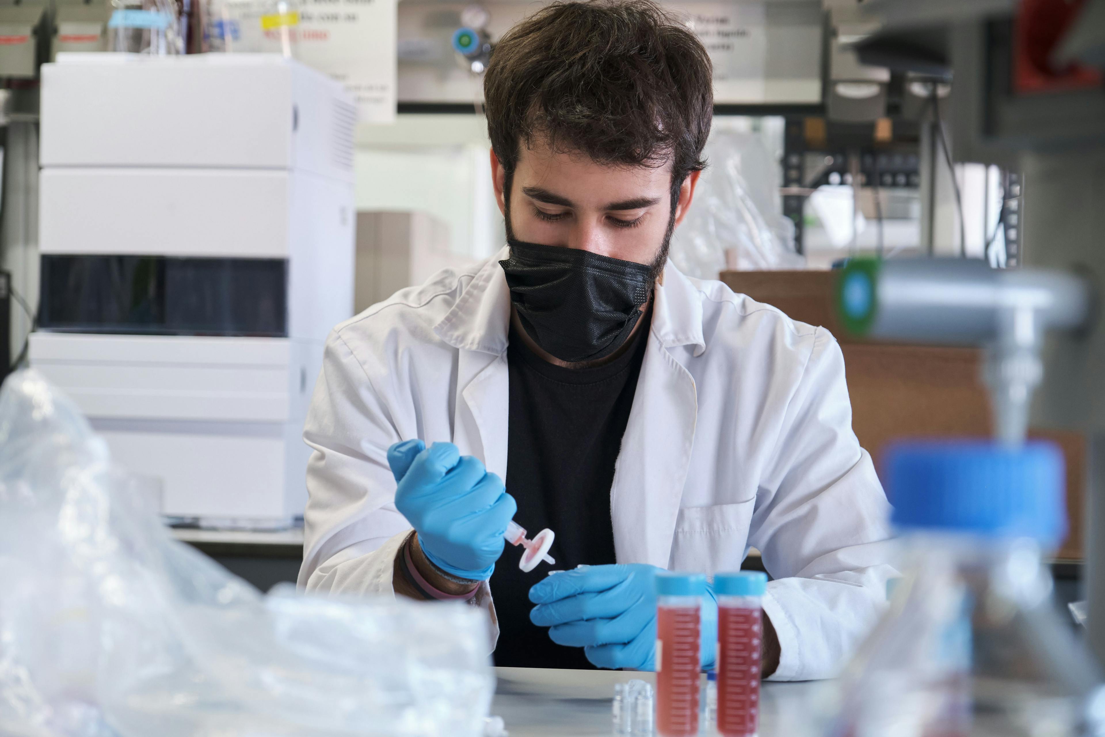 Scientist in white lab coat and protective face mask filter sample into HPLC vial. High performance liquid chromatography at chemical laboratory. | Image Credit: © Ladanifer - stock.adobe.com