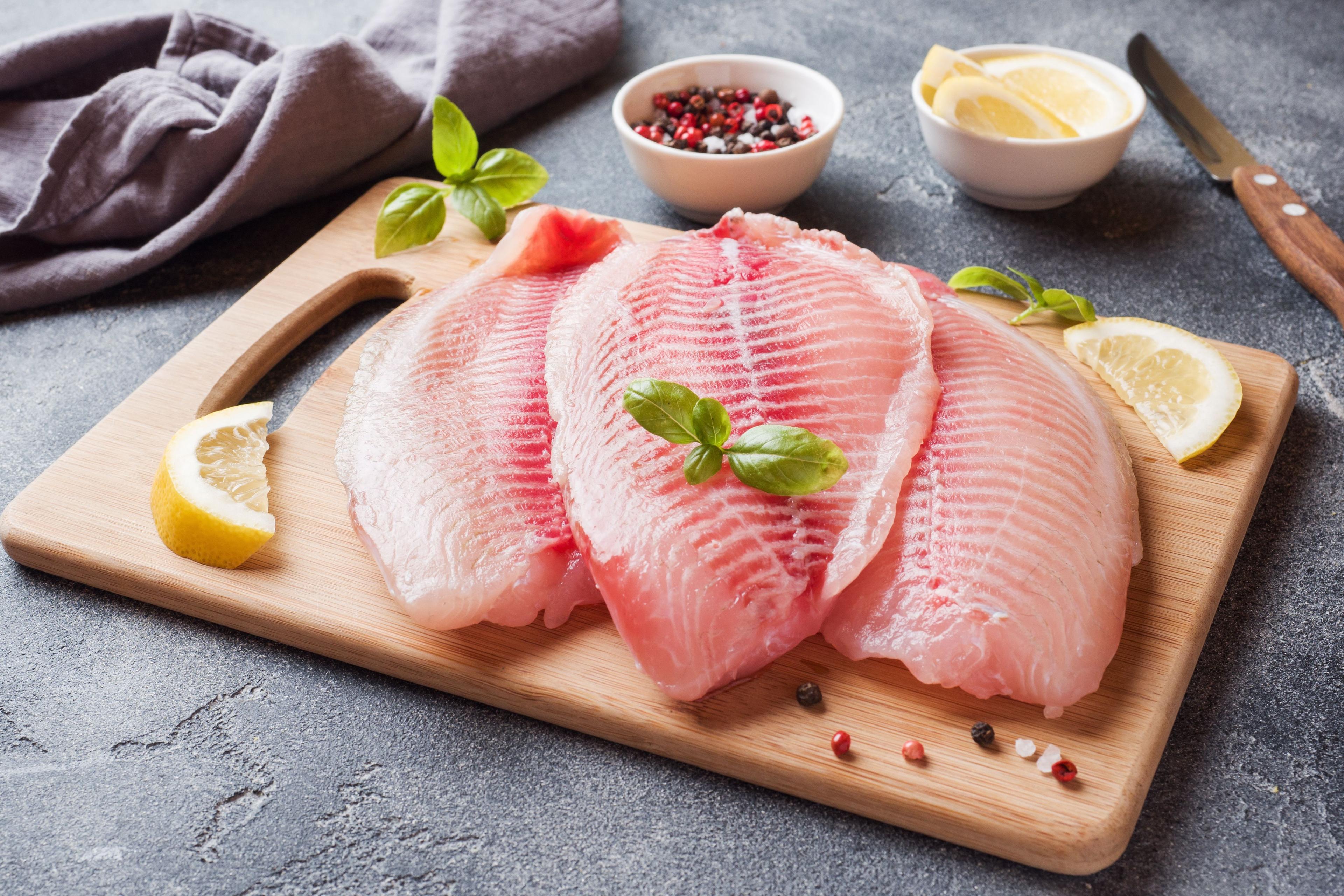 Raw fish fillet of tilapia on a cutting board with lemon and spices. © Elengush - stock.adobe.com