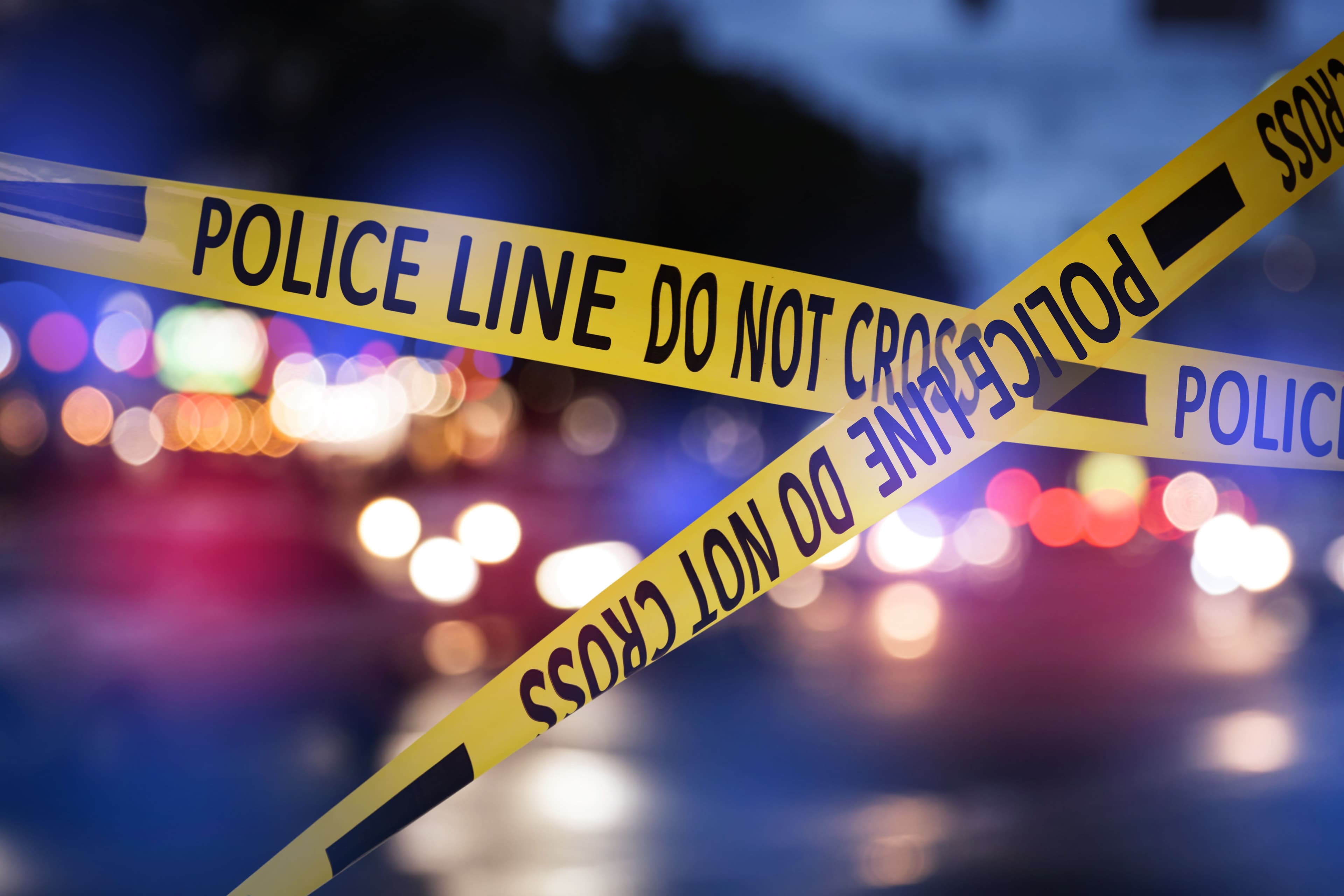 Crime scene with yellow police tape crisscrossing each other in the foreground. | Image Credit: © NewAfrica - stock.adobe.com